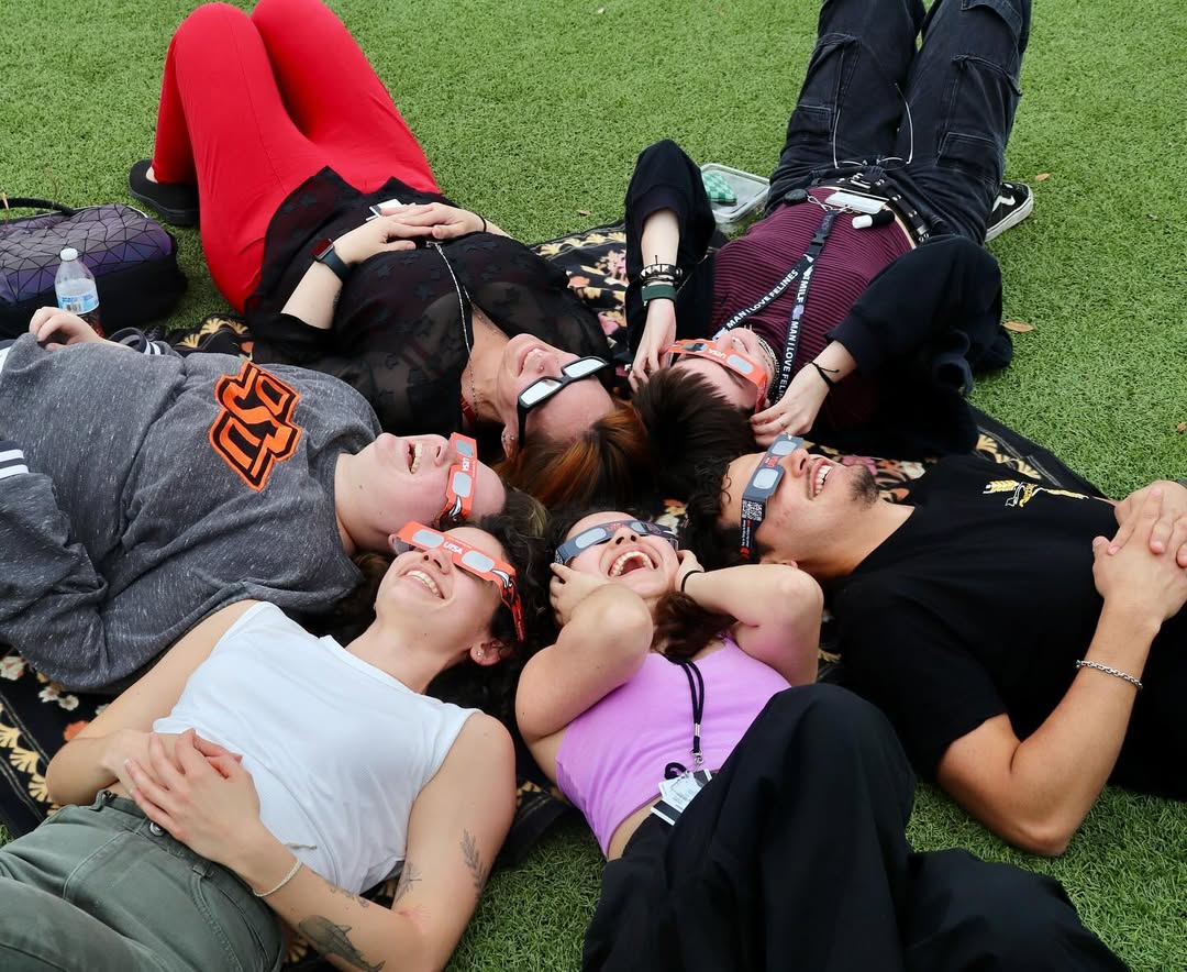 Students lying in a circle on the field at the UTSA Solar Eclipse viewing event, wearing eclipse glasses.